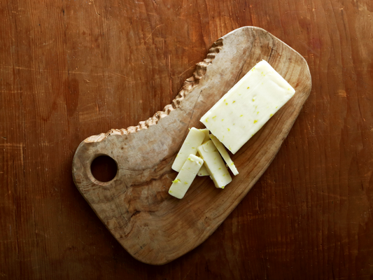 A 6oz block of Meister's Banana Pepper Jack cheese cut up on a wood cutting board showing the creamy Monterey Jack texture and bits of real zesty banana peppers.